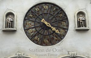 Grote ronde klok met glas-in-lood effect en klokluiders bij Station de Oost